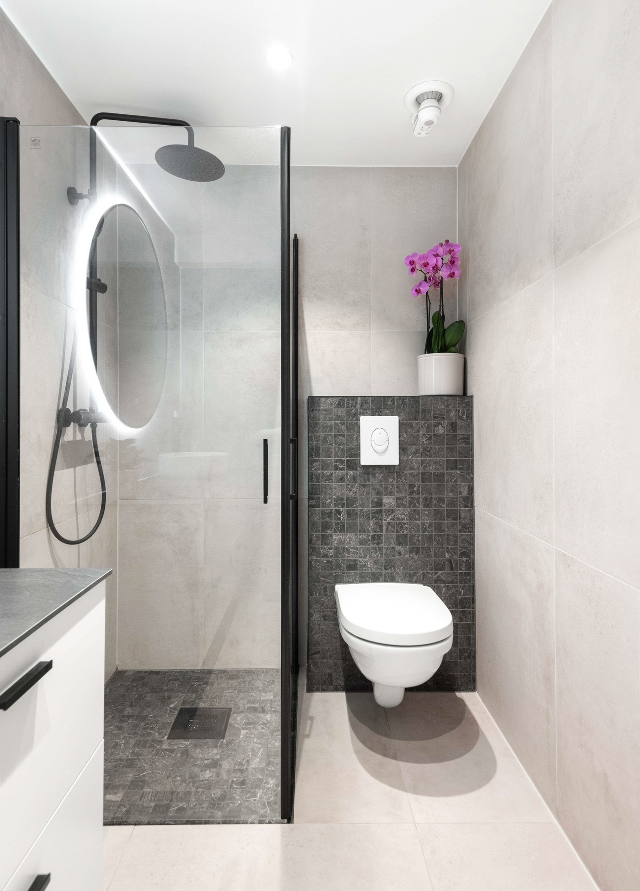 I hjørnet på badet er det en elegant dusjløsning med svarte detaljer og en veggmontert hånddusj med regnfallsfunksjon. Galleribilde