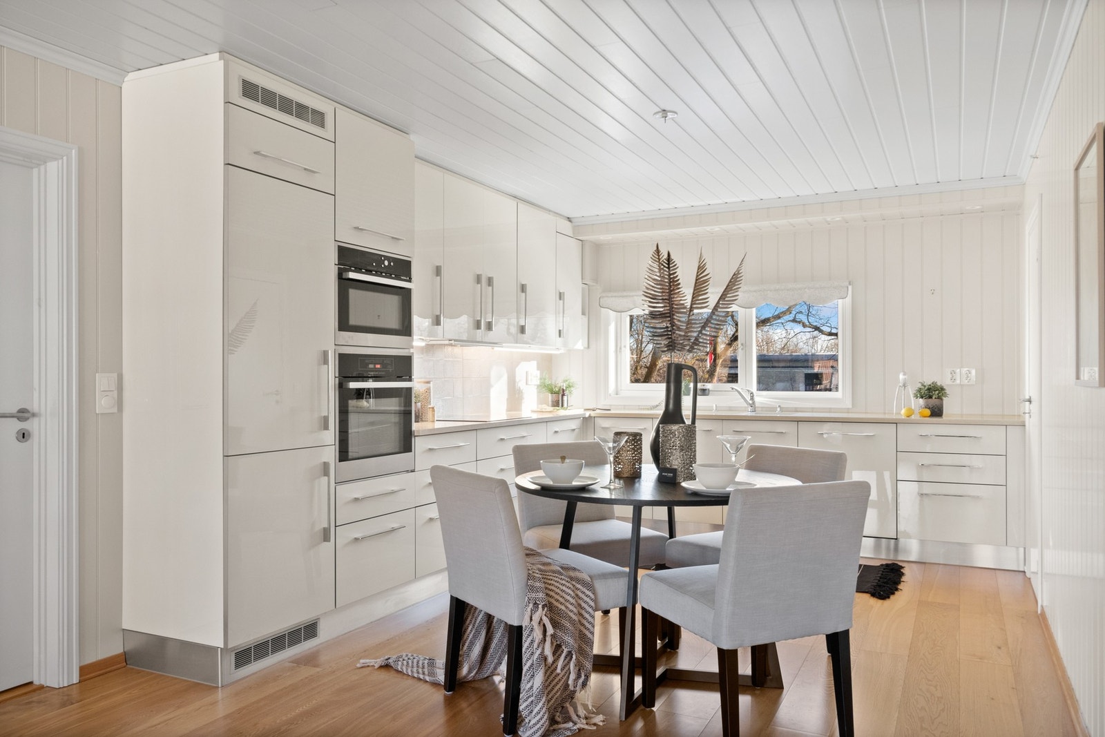 Kjøkkeninnredningen er oppført i en funksjonell L-form, med hvite, glatte fronter og dobbel oppvaskkum i en benkeplate av steinkompositt. Galleribilde