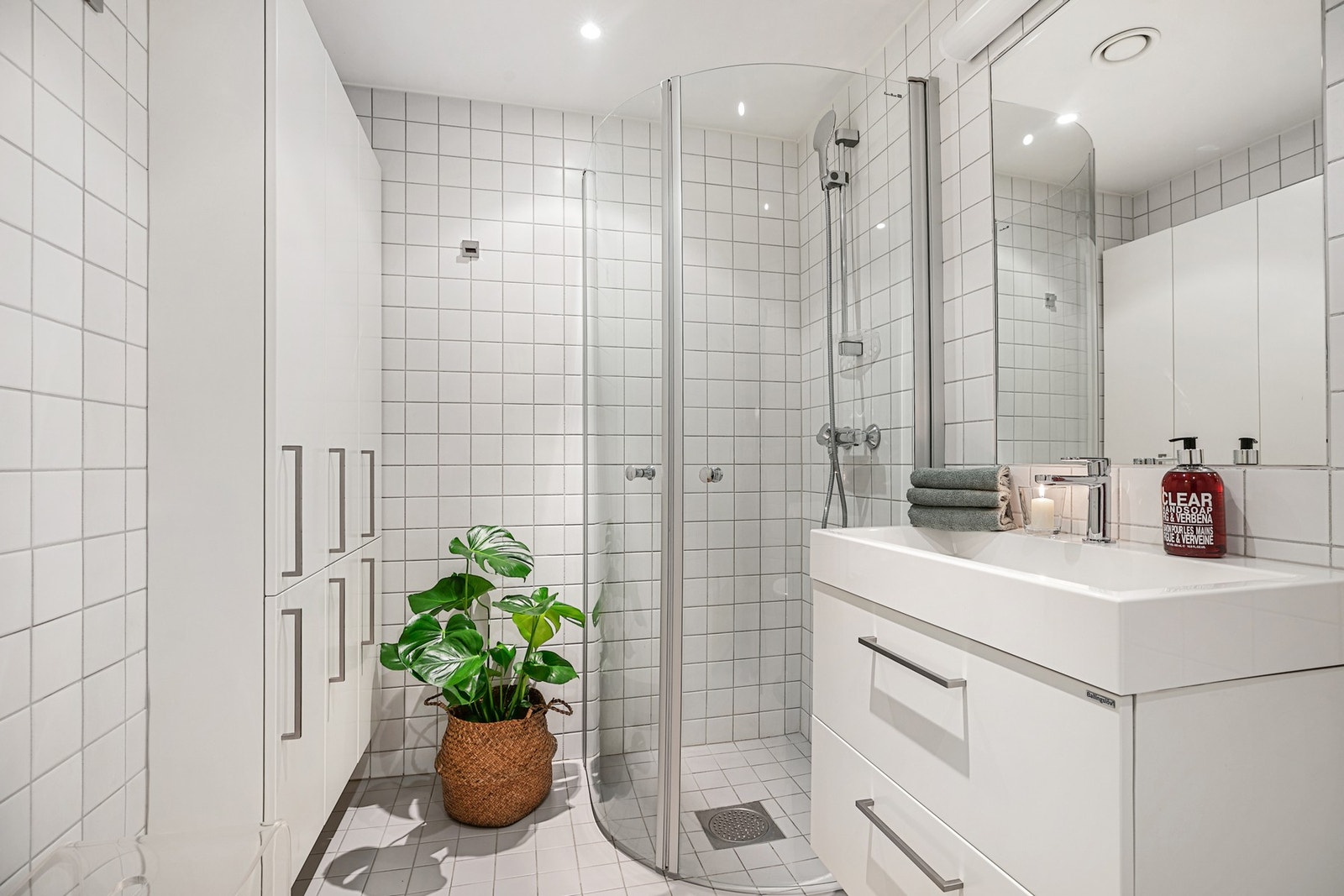 Et bad fra byggeår er innredet med servant, skuffeseksjon, stort veggskap, toalett og et dusjhjørne med buede glassdører Galleribilde