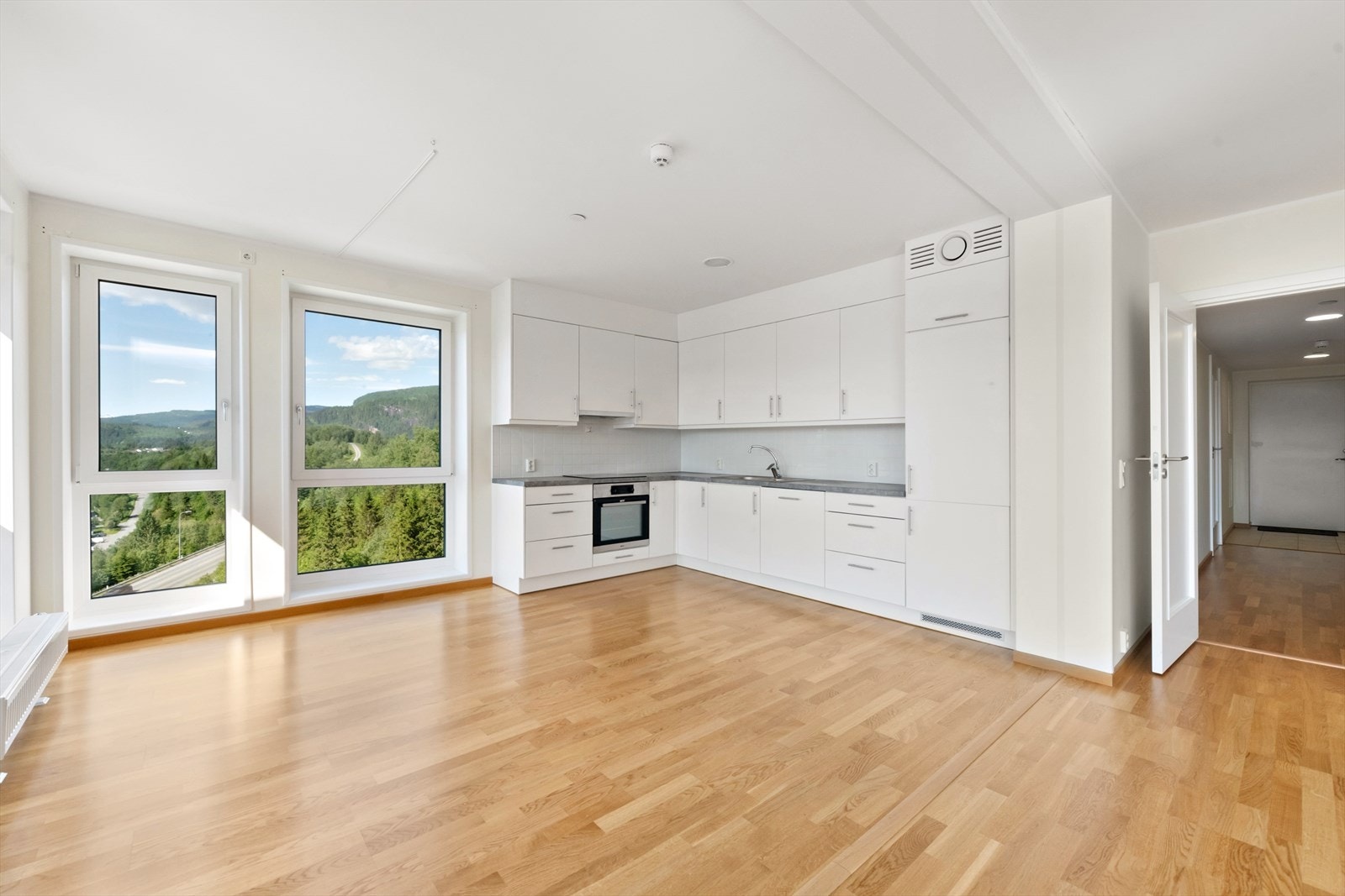 Kjøkkenet har innredning med slette fronter, og benkeplate av laminat med 2-kums benkebeslag. Kjøkkenet er lyst og har hvite fliser mellom benk og overskap. Det er L-formet, og har et tidløst uttrykk. Galleribilde