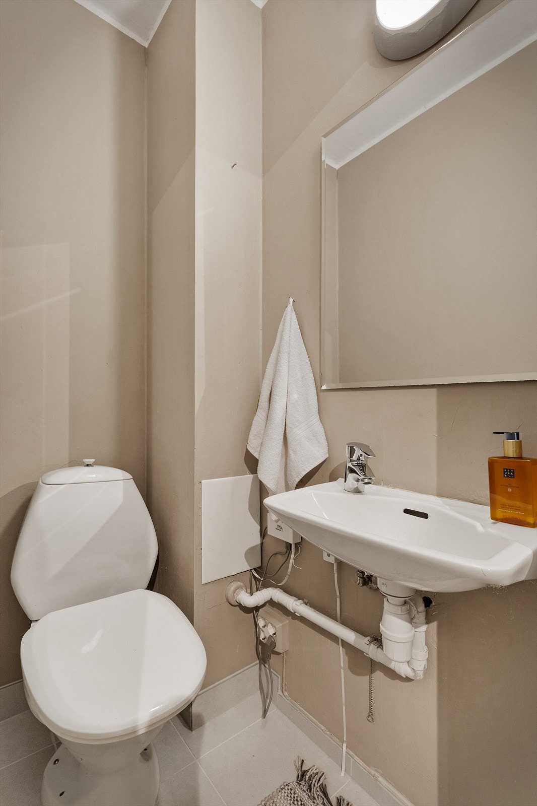 Praktisk toalettrom med flislagt gulv, toalett og enkel vask Galleribilde