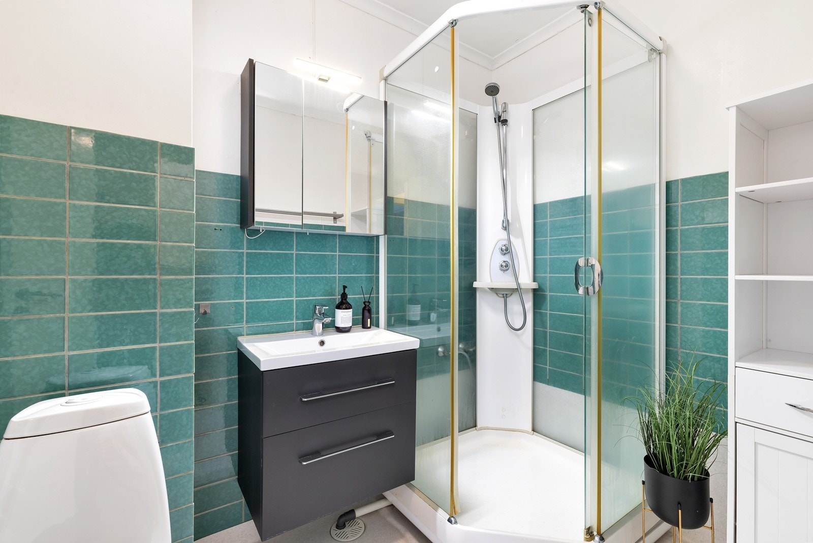 Bad med belegg på gulv og delvis flislagt på vegg. Badet har dusjkabinett, servant med underskuffer og toalett. Galleribilde