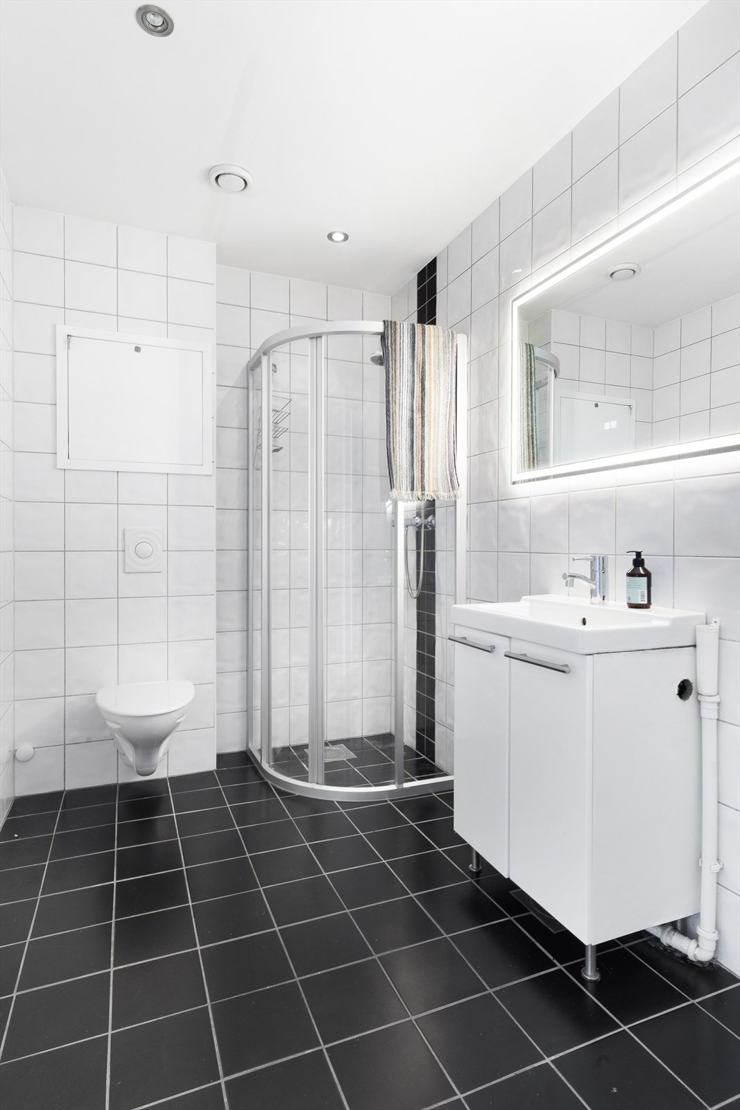 Badet er innredet med vegghengt toalett, servant i baderoms møblement, dusjhjørne med glassdører. Galleribilde