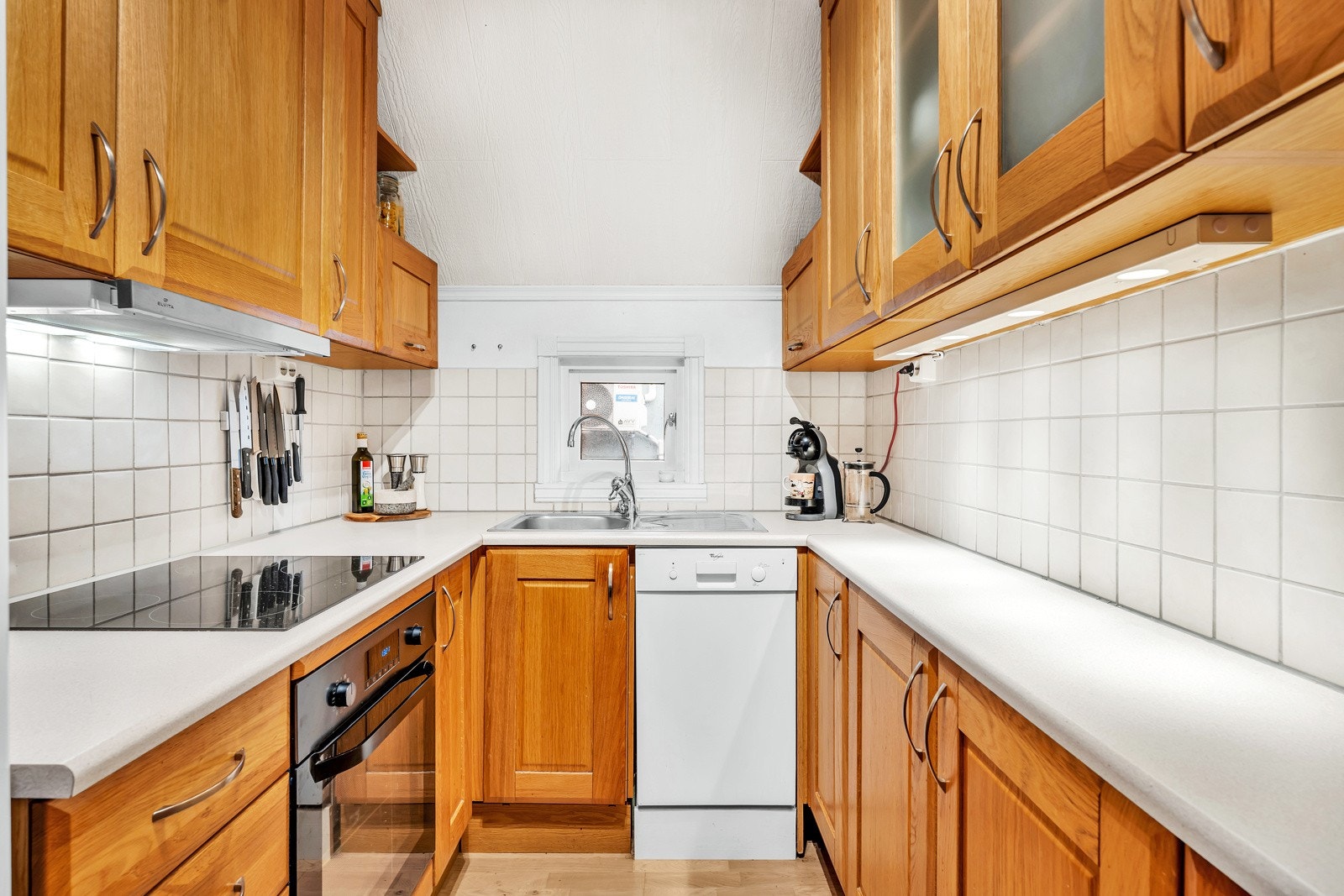 Kjøkkeninnredning med takhøye overskap, laminat benkeplate, fliser over benk og integrert stekeovn og induksjon platetopp. Galleribilde