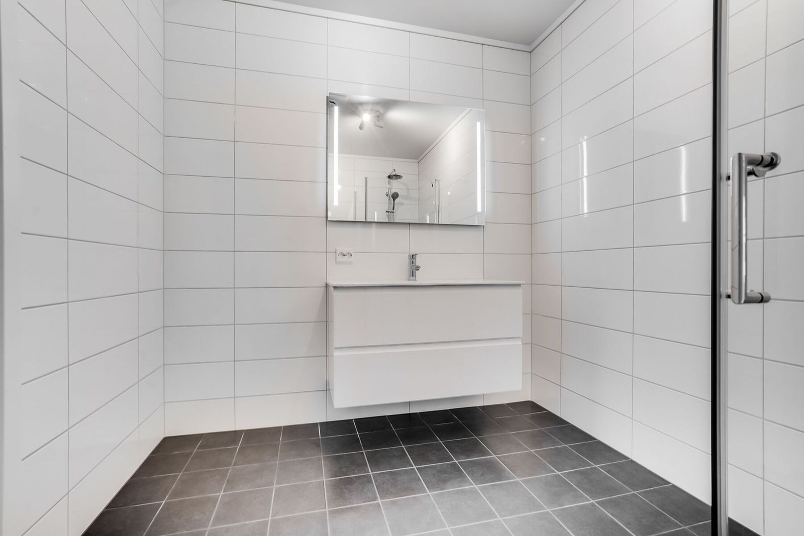 Badet er innredet med med servant, speil med lys, dusjhjørne og vegghengt toalett. Galleribilde