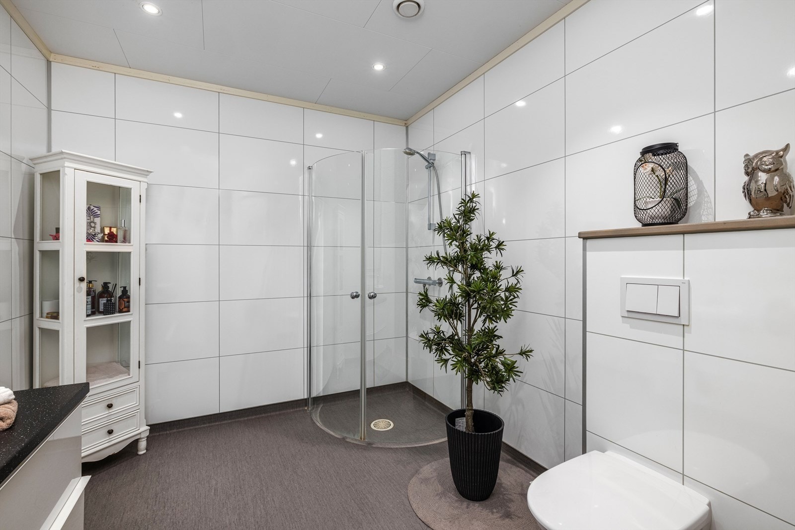 Gjestebad innredet med veggmontert toalett, servant på innredning og dusjhjørne med glassdører. Galleribilde