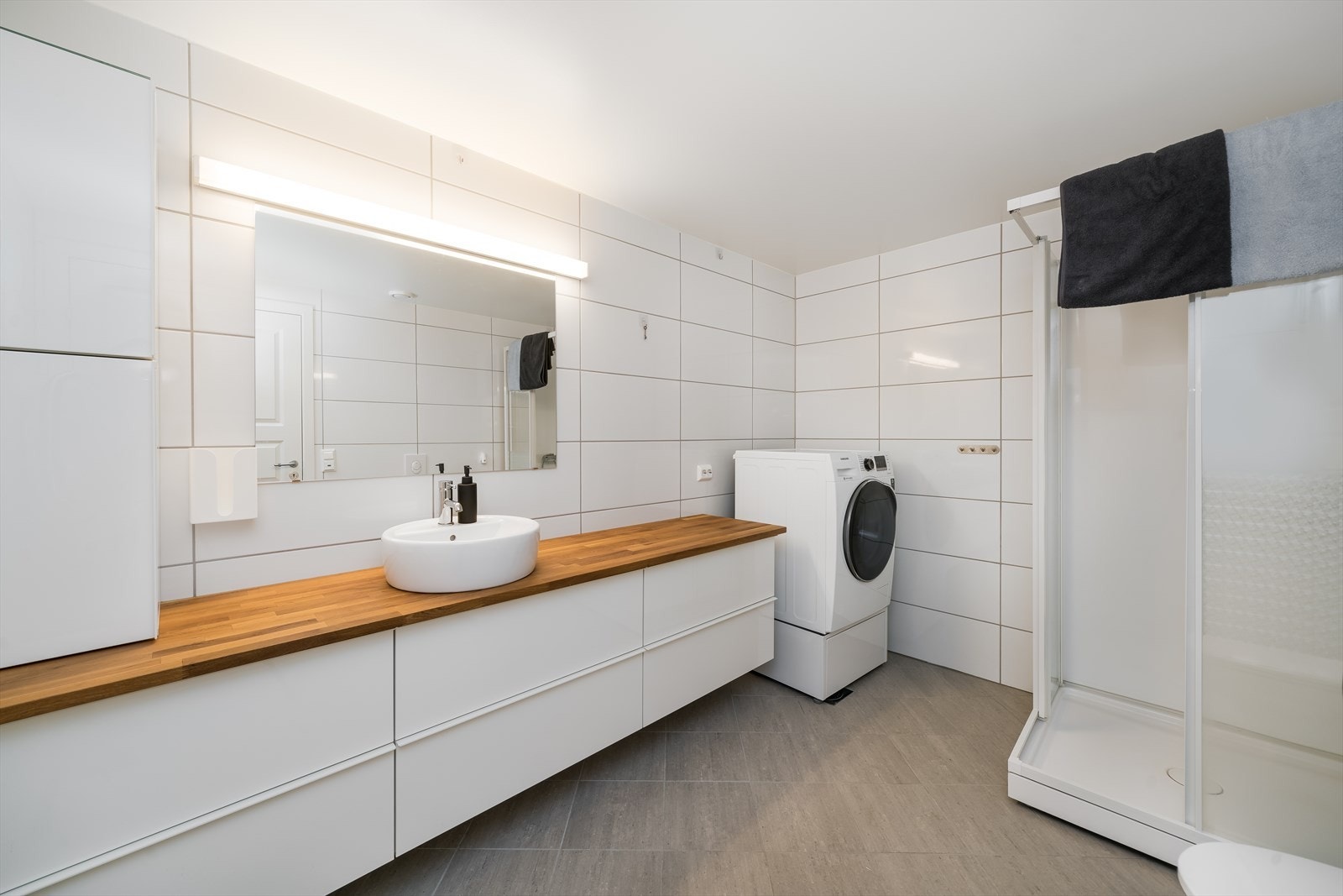 Pent kombinert bad og vaskerom i underetasjen. Badet er fliselagt og har varmekabler i gulv. Badet er innredet med baderomsinnredning med ekstra benk, toalett, dusjkabinett og opplegg til vaskemaskin. Galleribilde