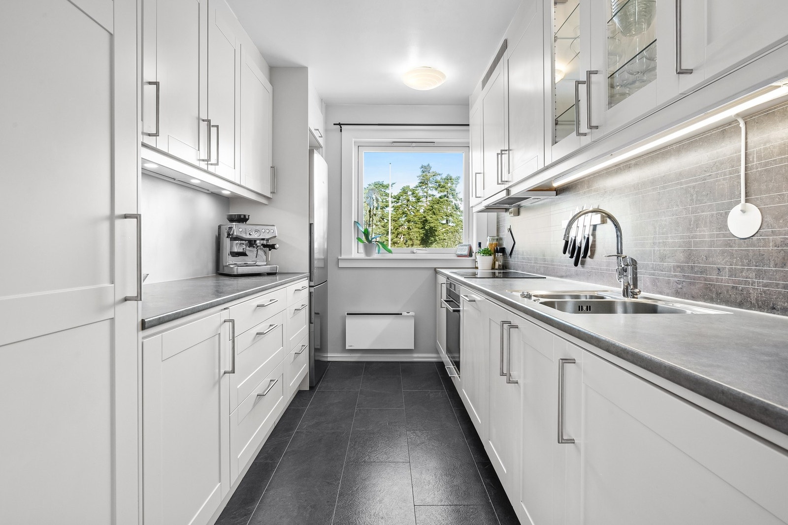 Kjøkkenet ligger i eget rom med nordvendt vindu og inngang fra entreen. Innredningen fra 2014 er plassert parallelt langs to sider med takoppforede overskap. Galleribilde