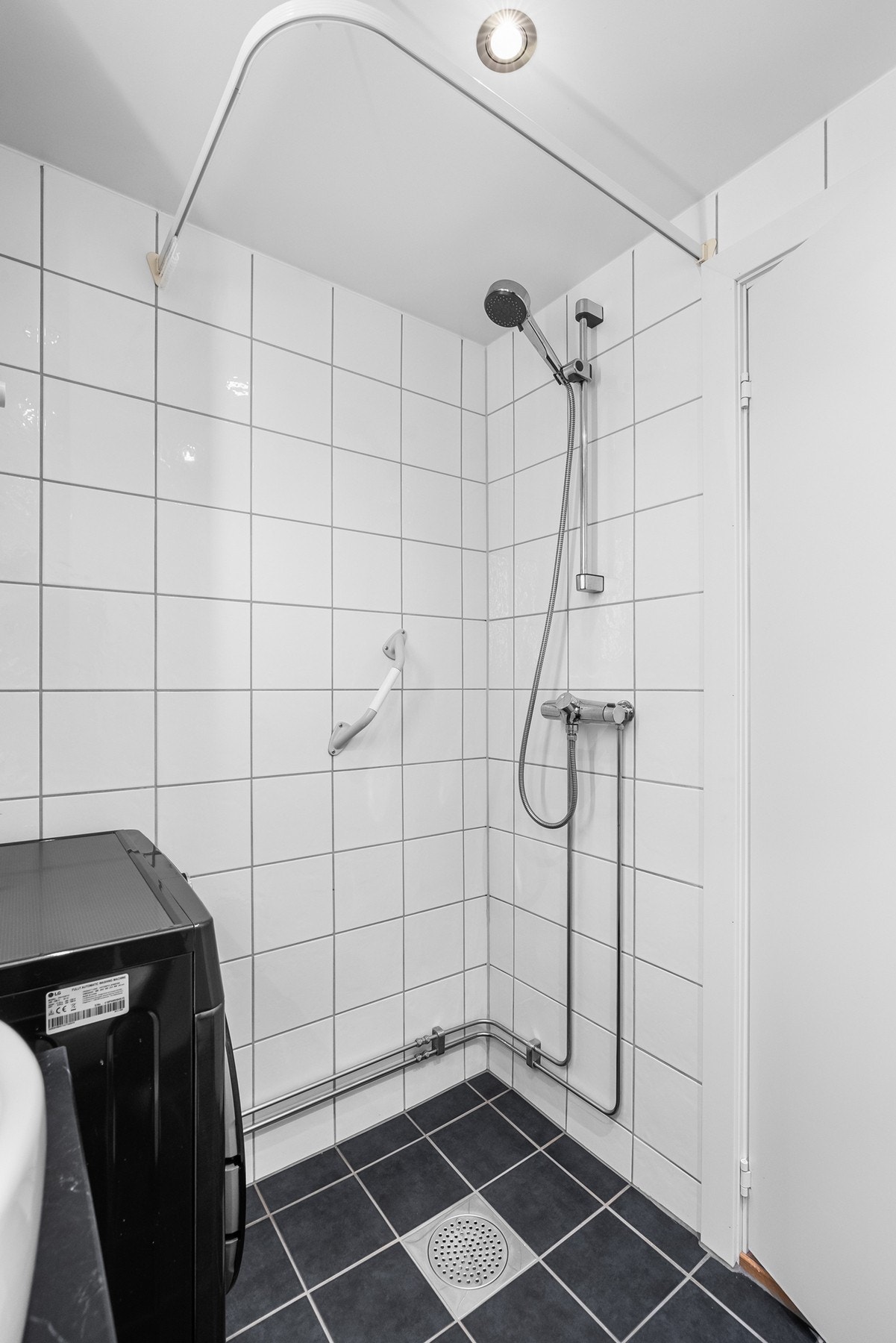 I hjørnet av rommet er det dusjhjørne og opplegg for vaskemaskin under en nyere, vegghengt varmtvannsbereder fra 2021. Galleribilde