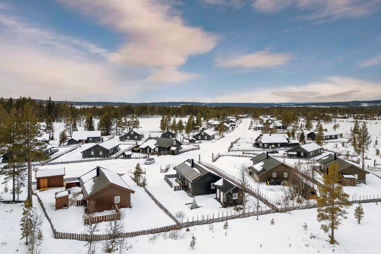 Snødekt hyttefelt med flere hytter, omringet av skog og fjell. Galleribilde