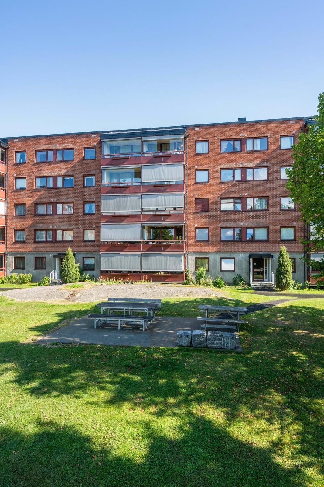 Fasade på sommertid. Store grøntarealer mellom blokkene, grillstasjoner og utegym. Galleribilde