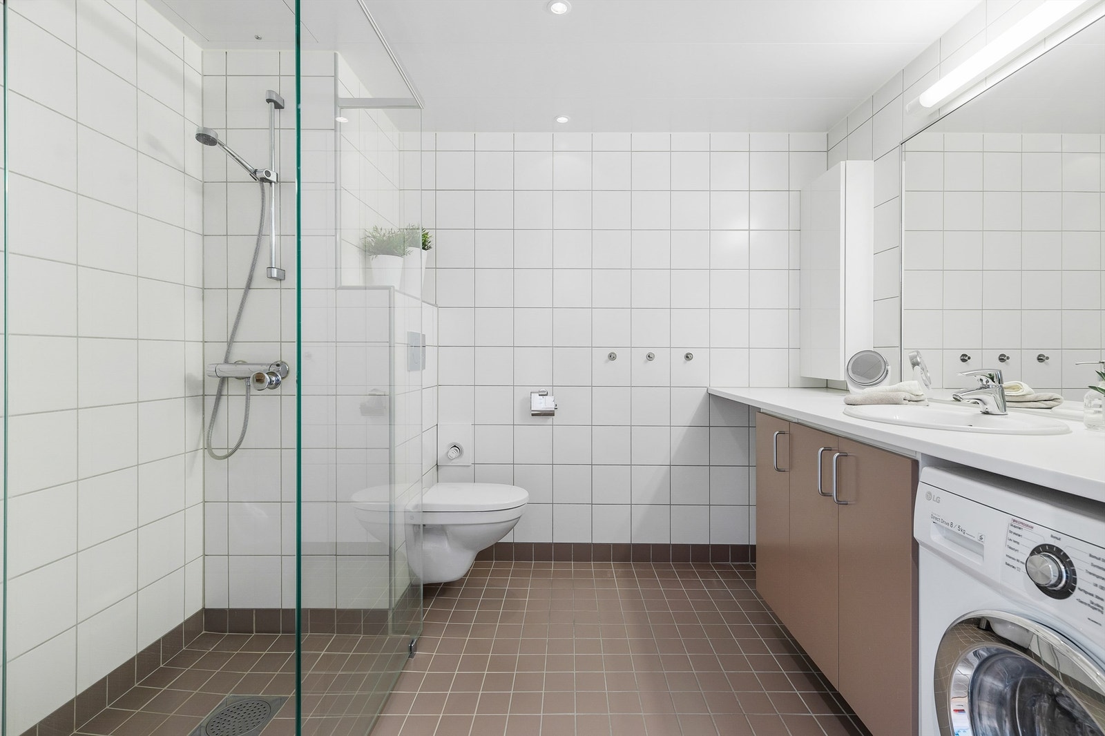 Baderomsmodul fra byggeår. Flislagt gulv med gulvvarme. Flislagte vegger. Nedsenket himling med lakkerte metallplater og downlights. Vegghengt servantskap med dører. Vegghengt toalett med innebygget sisterne. Galleribilde