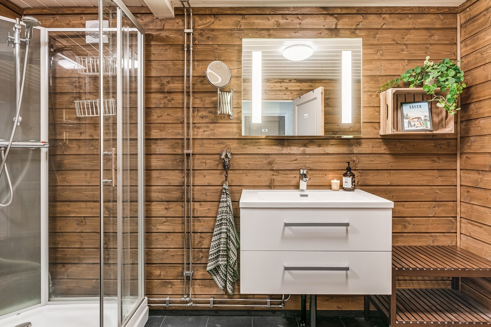 Badet fra 2014 har fliser på gulv med varmekabler under og beiset trepanel på vegger. Her er det god omkledningsplass. Nyere og moderne innredning med dusjkabinett, samt heldekkende servant og speil med belysning over. Galleribilde