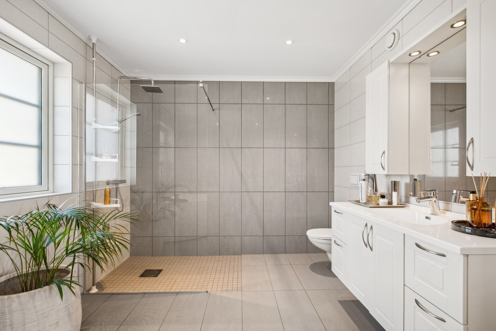 Her er det også et rålekkert, flislagt bad. Det er nedsenket dusjsone med glassdør, servatinnredning med speilskap, vegghengt toalett og badekar. Galleribilde