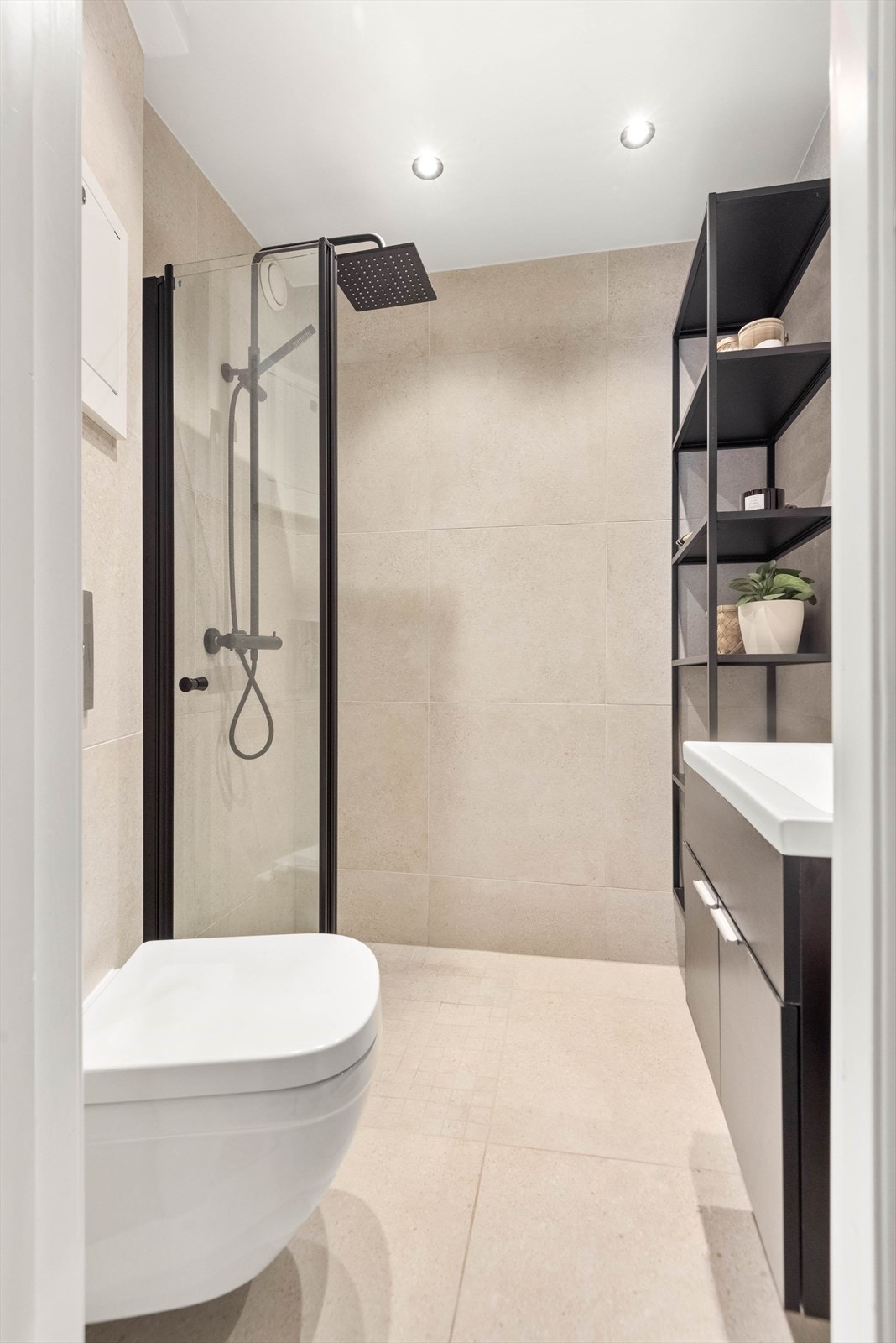 Nyoppusset bad fra 2022, fliser og varme i gulv. Vegger og malt himling med downlights. Badet er innredet med hylle, dusjhjørne og foldbar dusjdør. Galleribilde