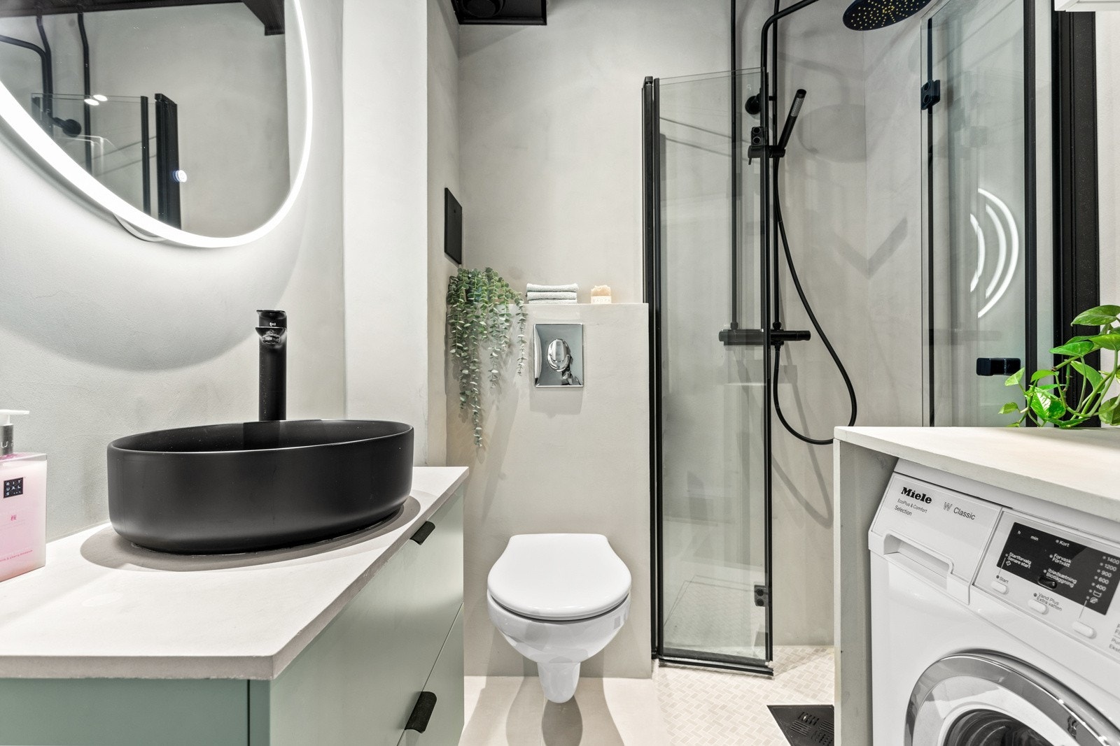 Videre har badet et vegghengt toalett, opplegg for vaskemaskin og et dusjhjørne med regnfallsdusj og innfellbare glassdører. Galleribilde