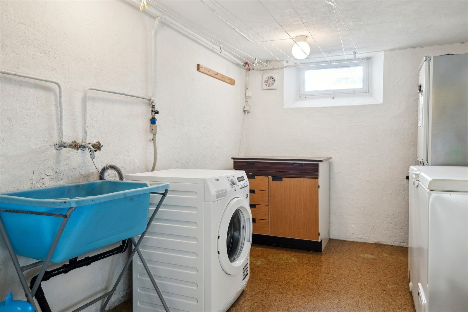 I boligen er det en praktisk vaskekjeller med belegg på gulv og malt betong på veggene. Det er skyllekar på stativ og opplegg for vaskemaskin. Galleribilde
