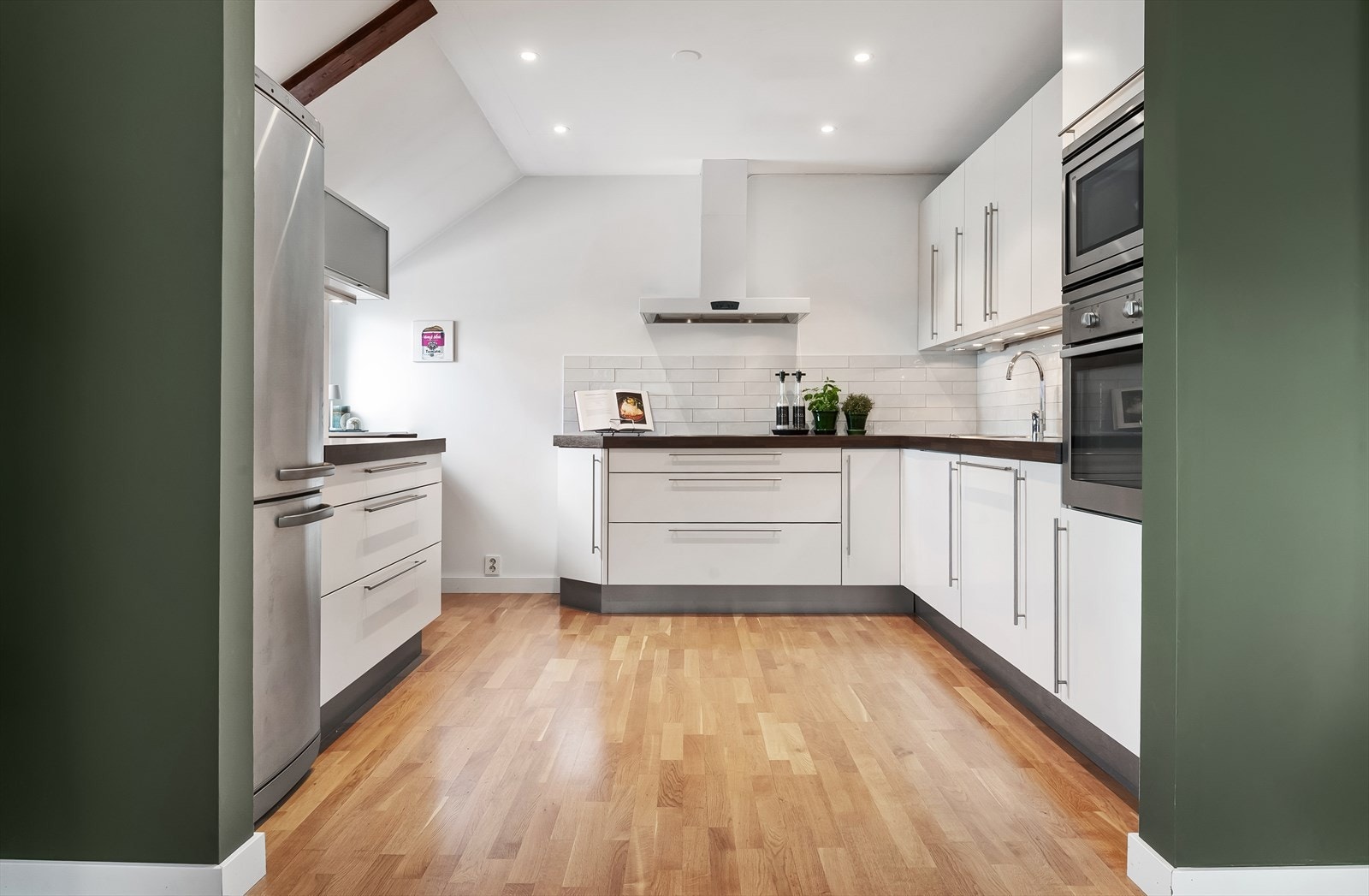 Velutstyrt kjøkken fra HTH med hvite folierte fronter, benkeplate med underlimt vaskekum og nedfelt keramisk platetopp. Over benk er det montert fliser. Galleribilde