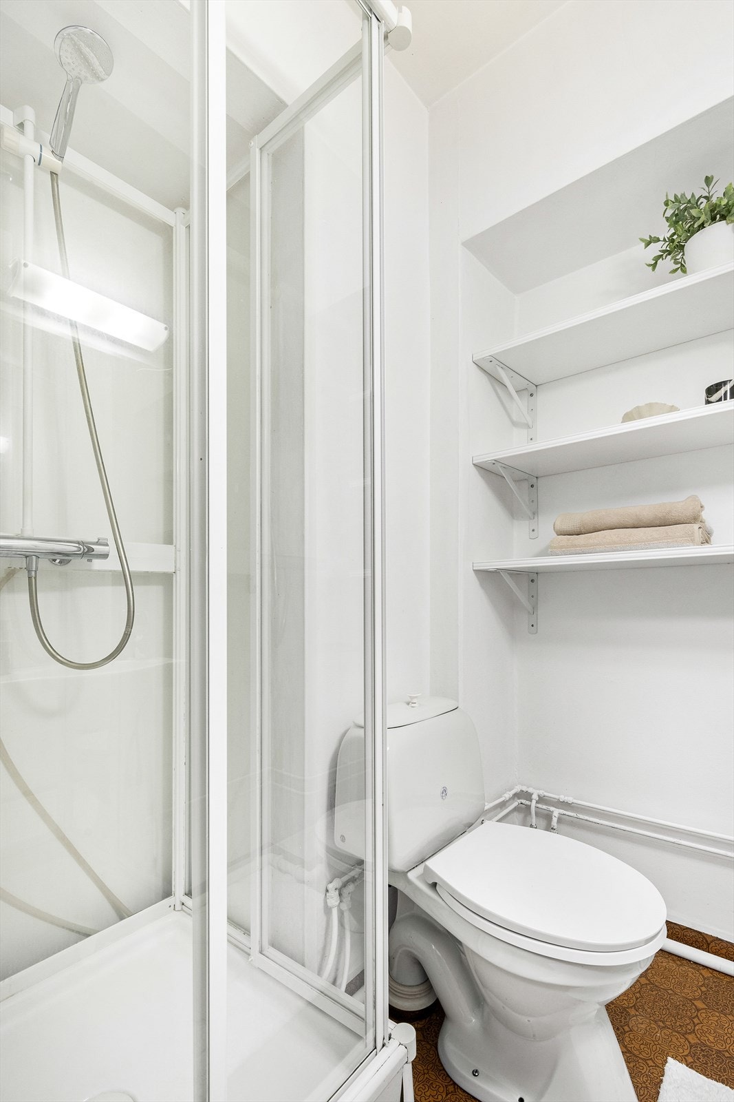 Badet er innredet med frittstående toalett, dusjkabinett, servant og speil med lys over. Galleribilde