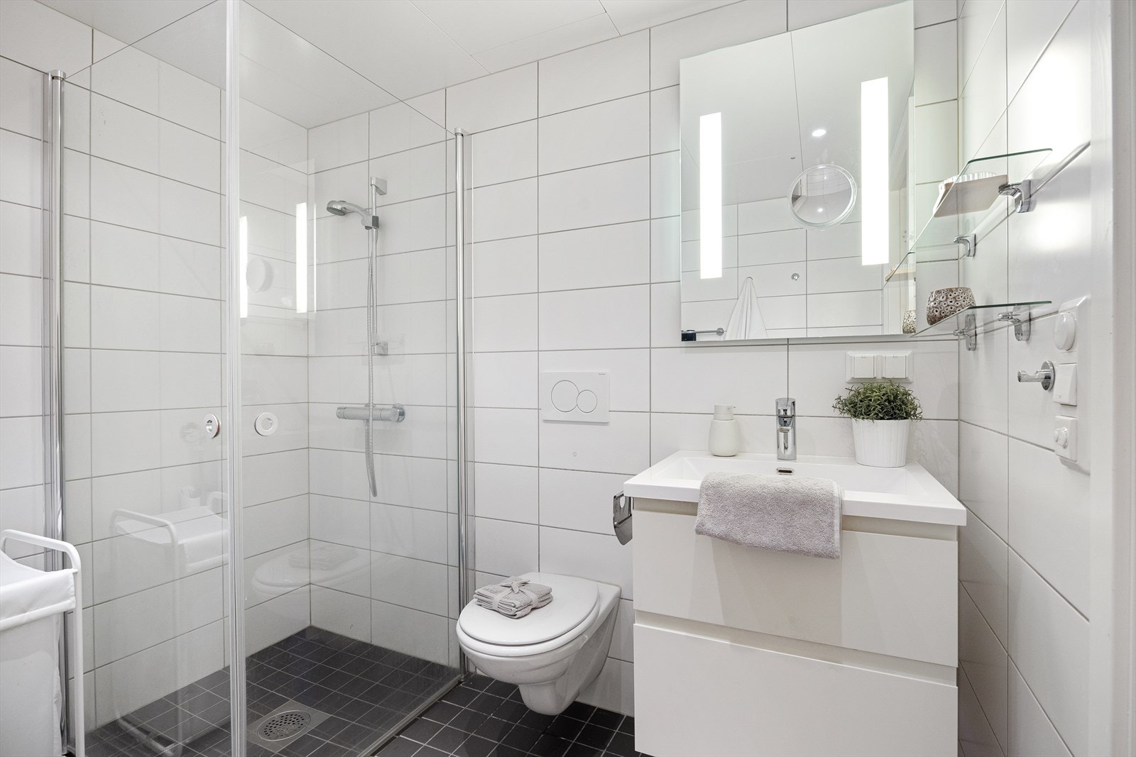 Badet er innredet med vegghengt klosett, servant på innredning og dusjarmatur med svingbare glassdører. Galleribilde