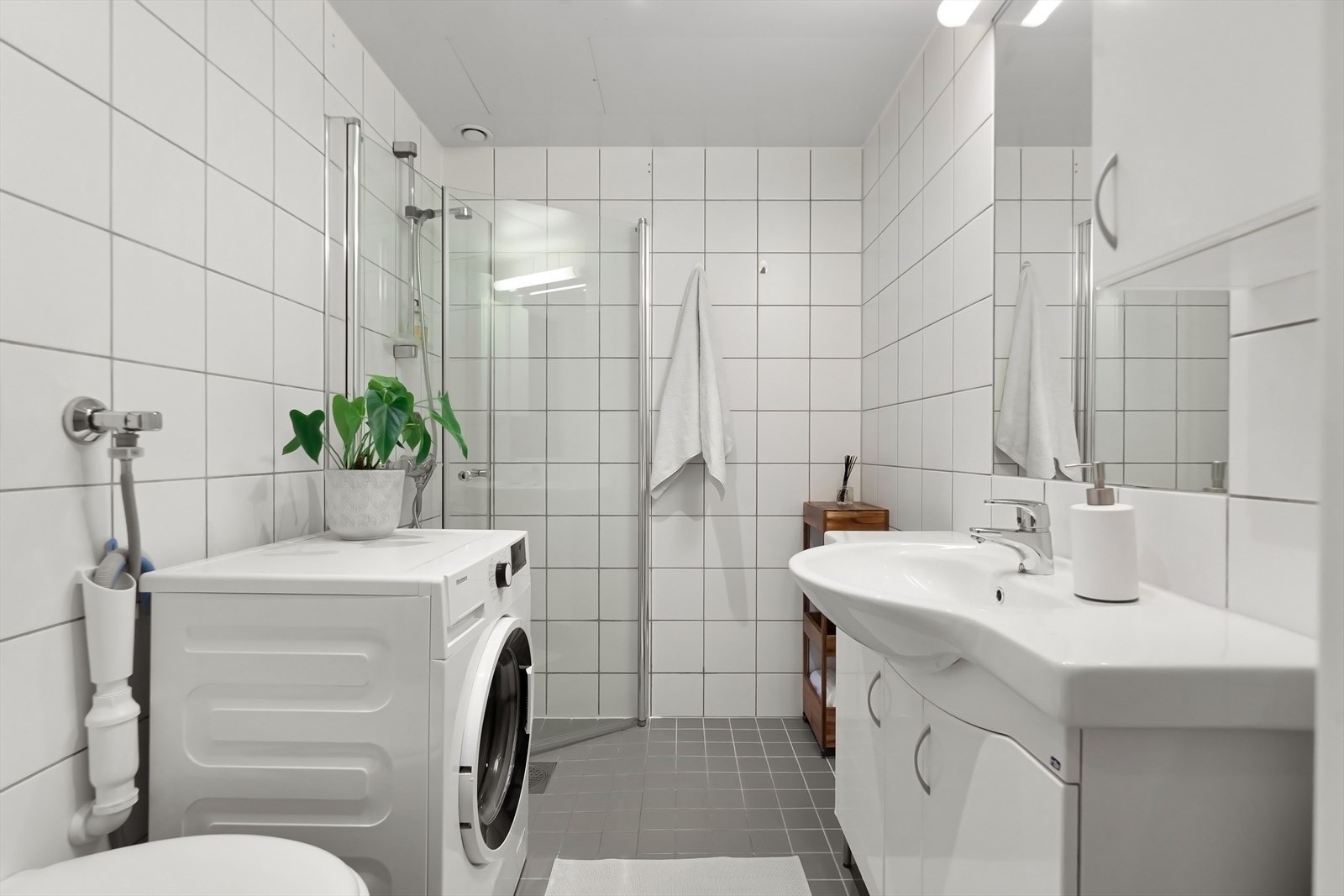 Romslig flislagt bad med dusjhjørne, servant, toalett samt opplegg til vaskemaskin Galleribilde