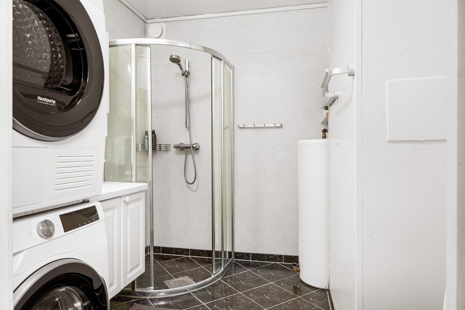 Badet er innredet med sorte gulvfliser og hvitt våtromsbelegg på veggene og dusjhjørne med skyvedører. Galleribilde