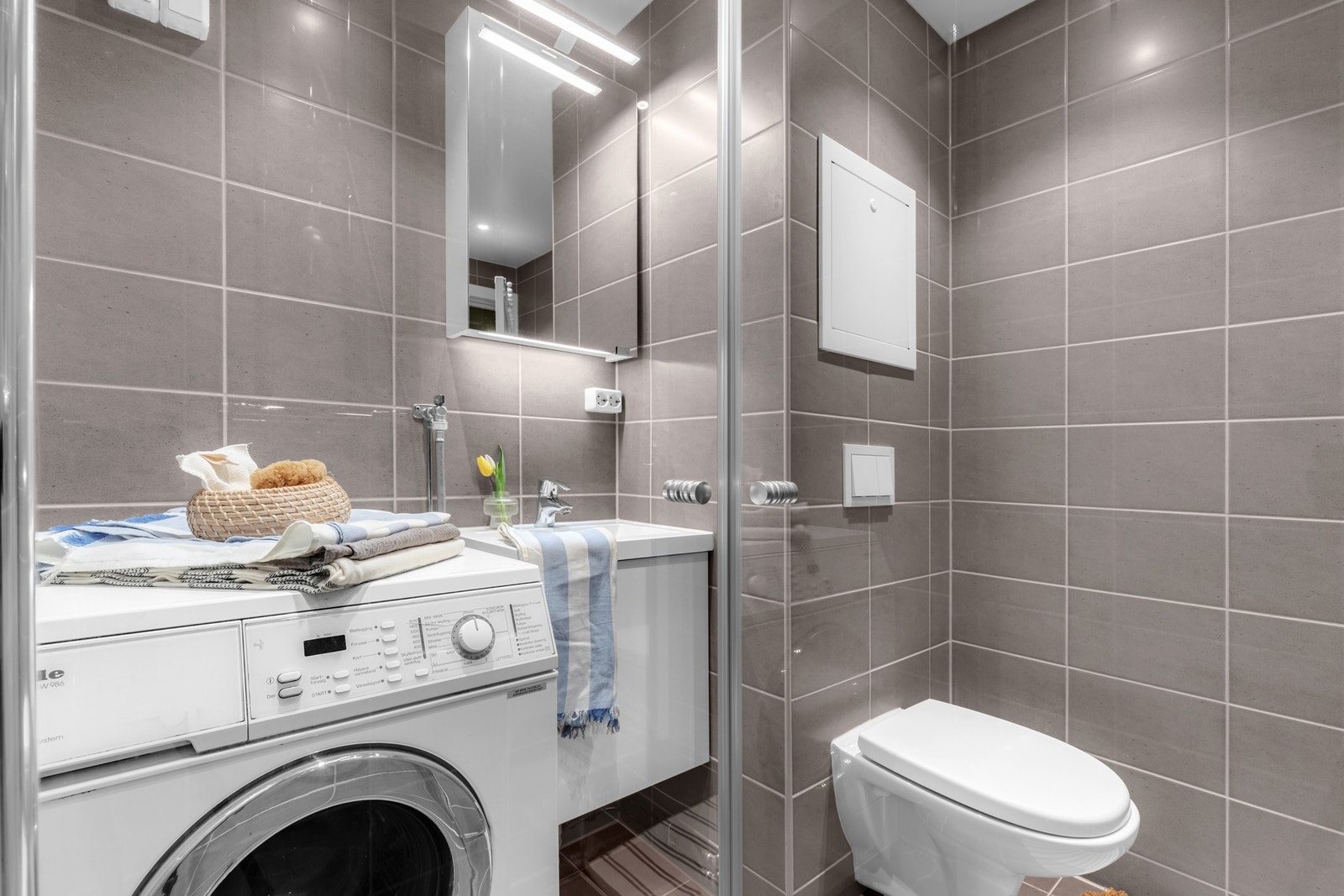 Dusjhjørnet med innfellbare glassdører gir en åpen og romslig følelse, mens det vegghengte toalettet og servantskapet sørger for en ren finish. Galleribilde