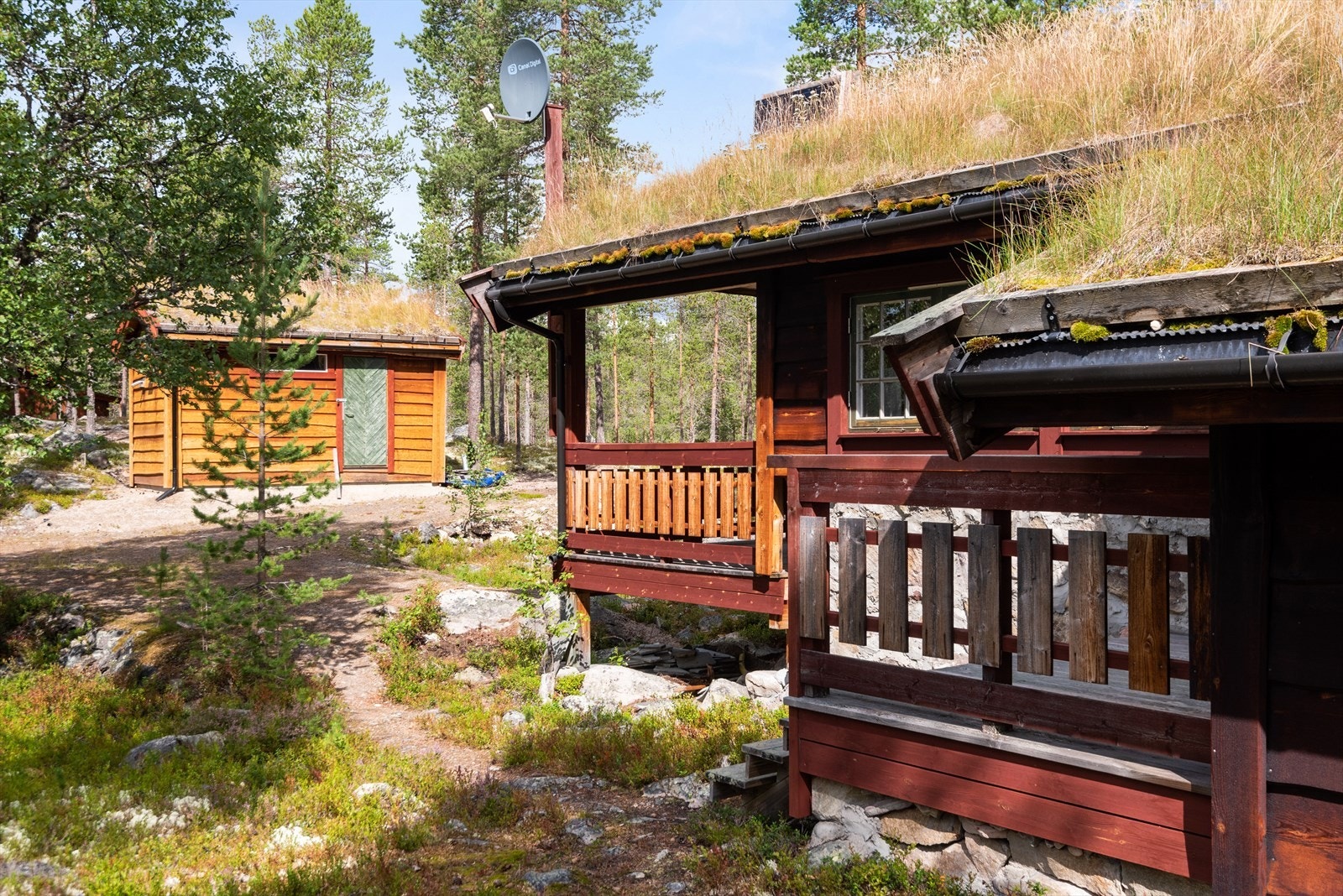 Hytta med overbygget inngangsparti, uthus/redskapsbod i bakgrunn. Galleribilde