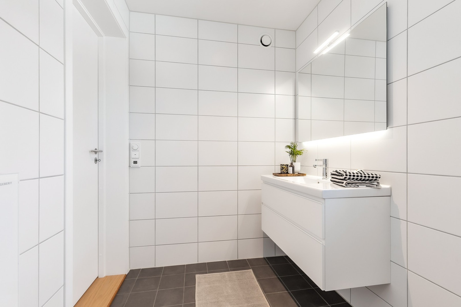 Rommet er innredet med vegghengt servantinnredning med skuffer, ovenpåliggende servant med ett-greps armatur og speil med overlys Galleribilde