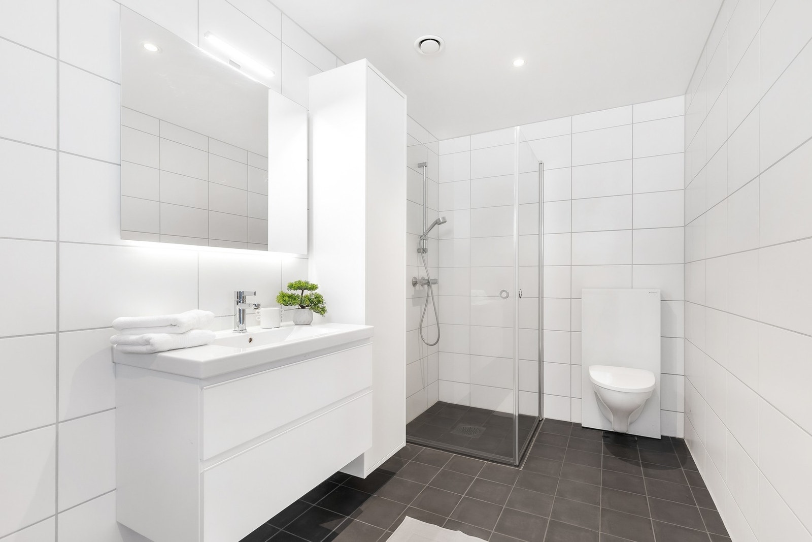 Rommet er utstyrt med vegghengt toalett, dusjhjørne, servantinnredning og opplegg for vaskemaskin og tørketrommel Galleribilde