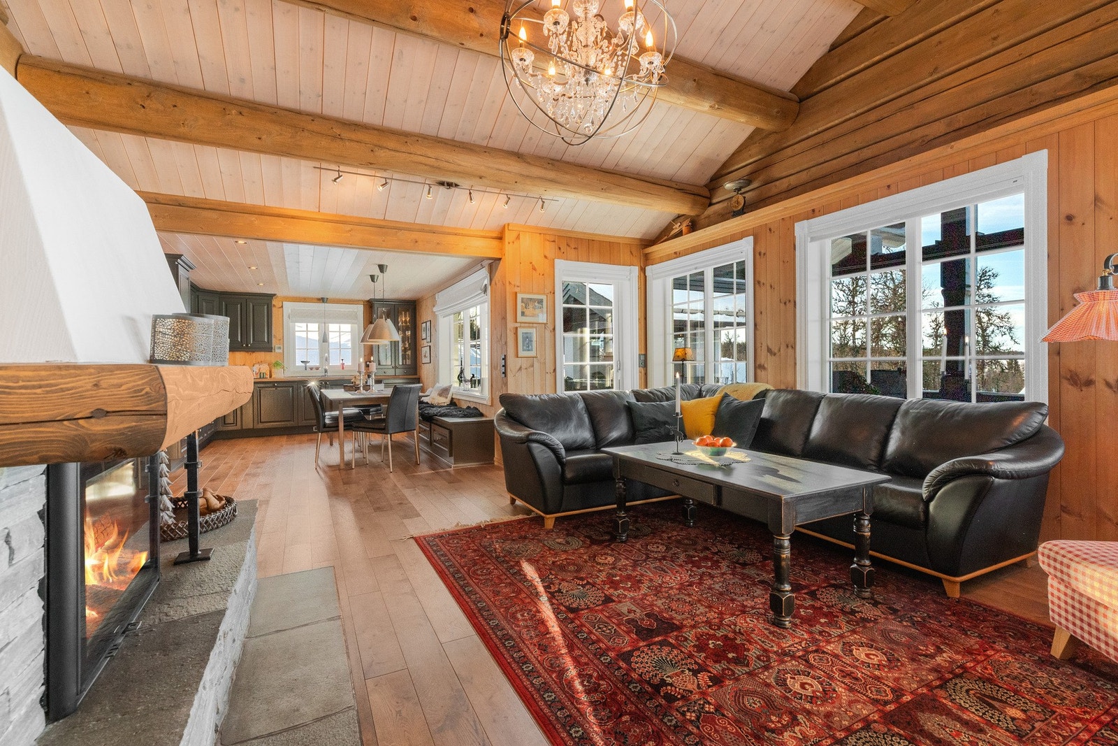 Stua har åpen og høy himling, tømmerdetaljer og en flott peis som skaper en lun og koselig atmosfære Galleribilde