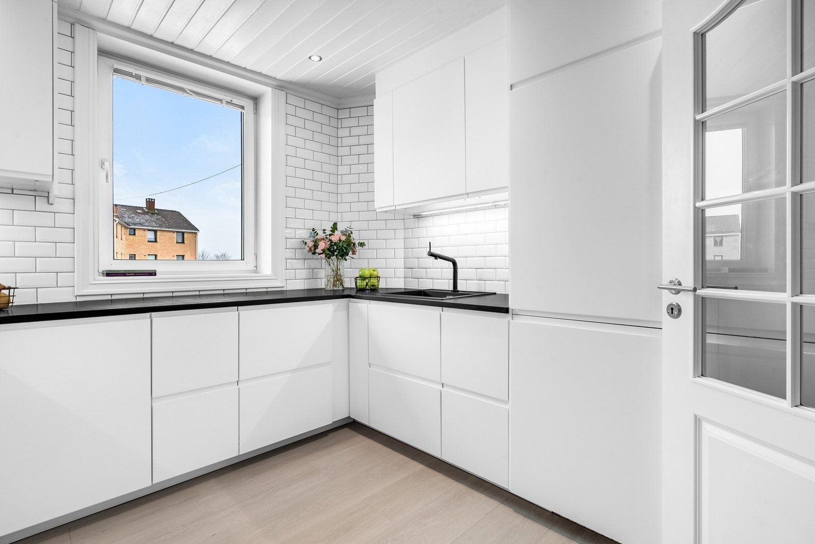 Glatte hvite fronter, sort laminat benkeplate med nedfelt kum i sort kompositt, sort blandebatteri, lys under overskap og hvitt flisfelt på vegg! Galleribilde