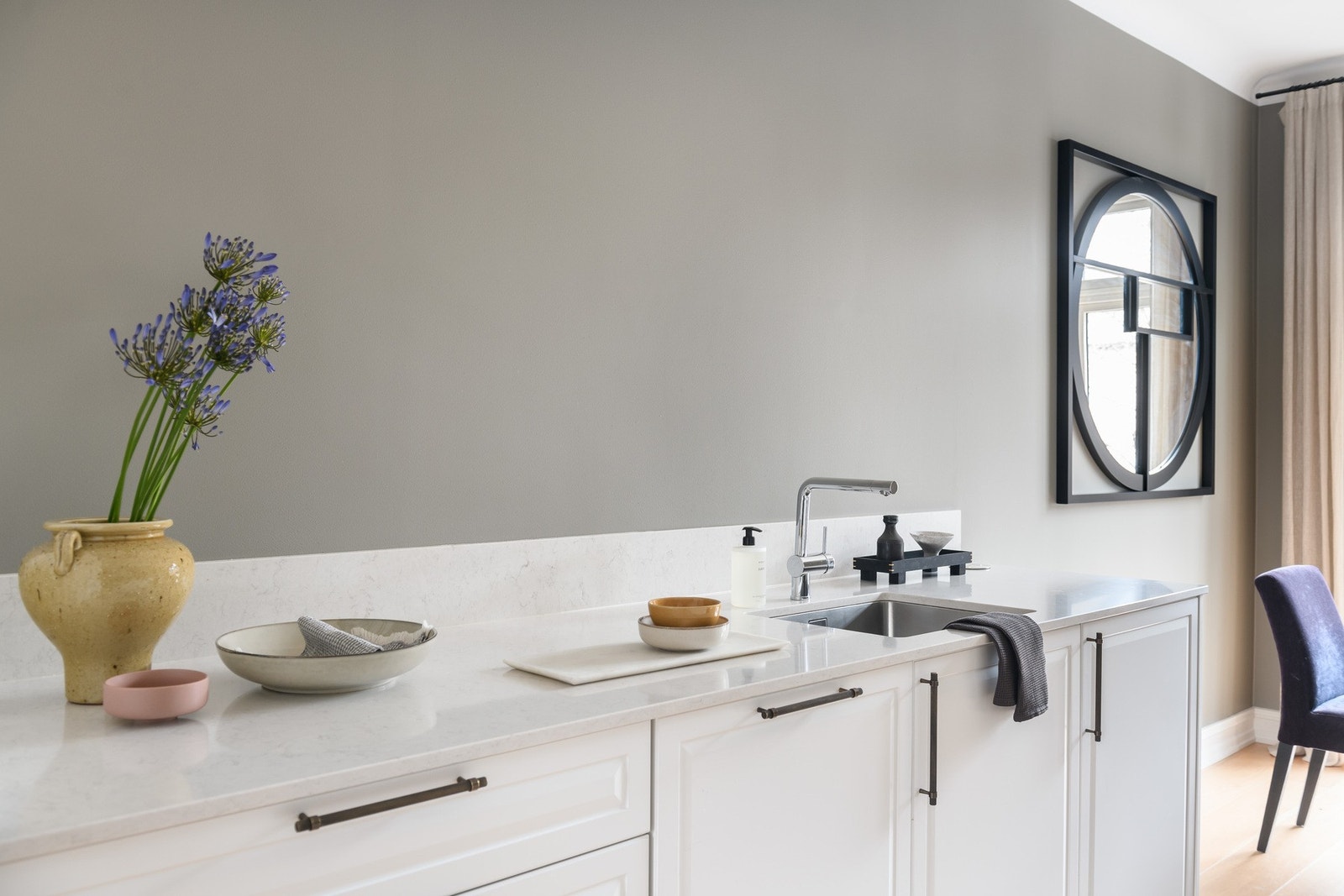 Innredning med hvite profilerte fronter med mørke håndtak fra Lovehandles. Lys benkeplate i komposittstein fra Sigvartsen med underlimt vaskekum. Galleribilde