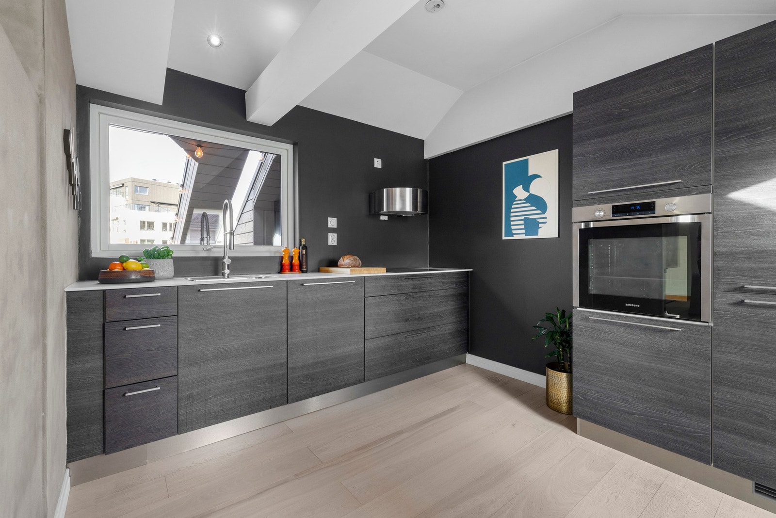 Lekkert KVIK kjøkken fra 2014 med mørke, glatte finerte fronter, laminat benkeplate med planlimt kum i rustfritt stål og veggmontert kullfilterventilator. Integrert innredning bestående av keramisk platetopp, stekeovn, oppvaskmaskin og kjøl/frys. Galleribilde