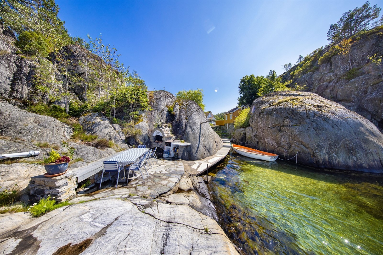 Den fine uteplassen ligger helt i sjøkanten med svaberg, badestige og skiferplatting med benk og oppmurt utepeis. Galleribilde