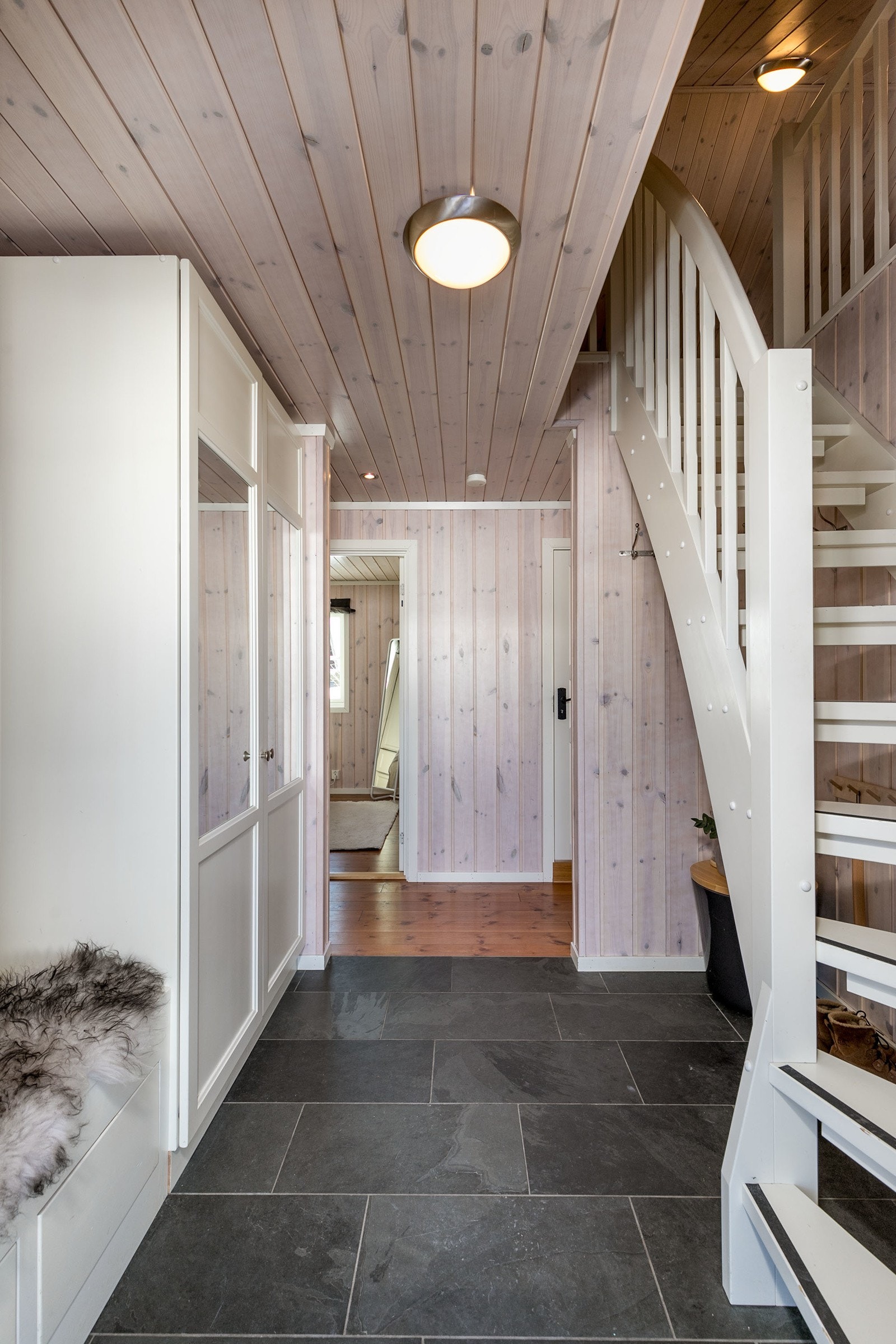 En romslig entre med skiferfliser på gulv og hvitpigmentert trepanel gir et godt førsteinntrykk av fritidsboligen. Galleribilde