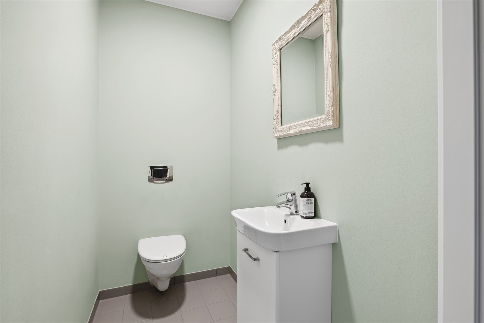 Gjestetoalettet har fliser på gulv og er innredet med vegghengt toalett, samt innredning med servant. Galleribilde