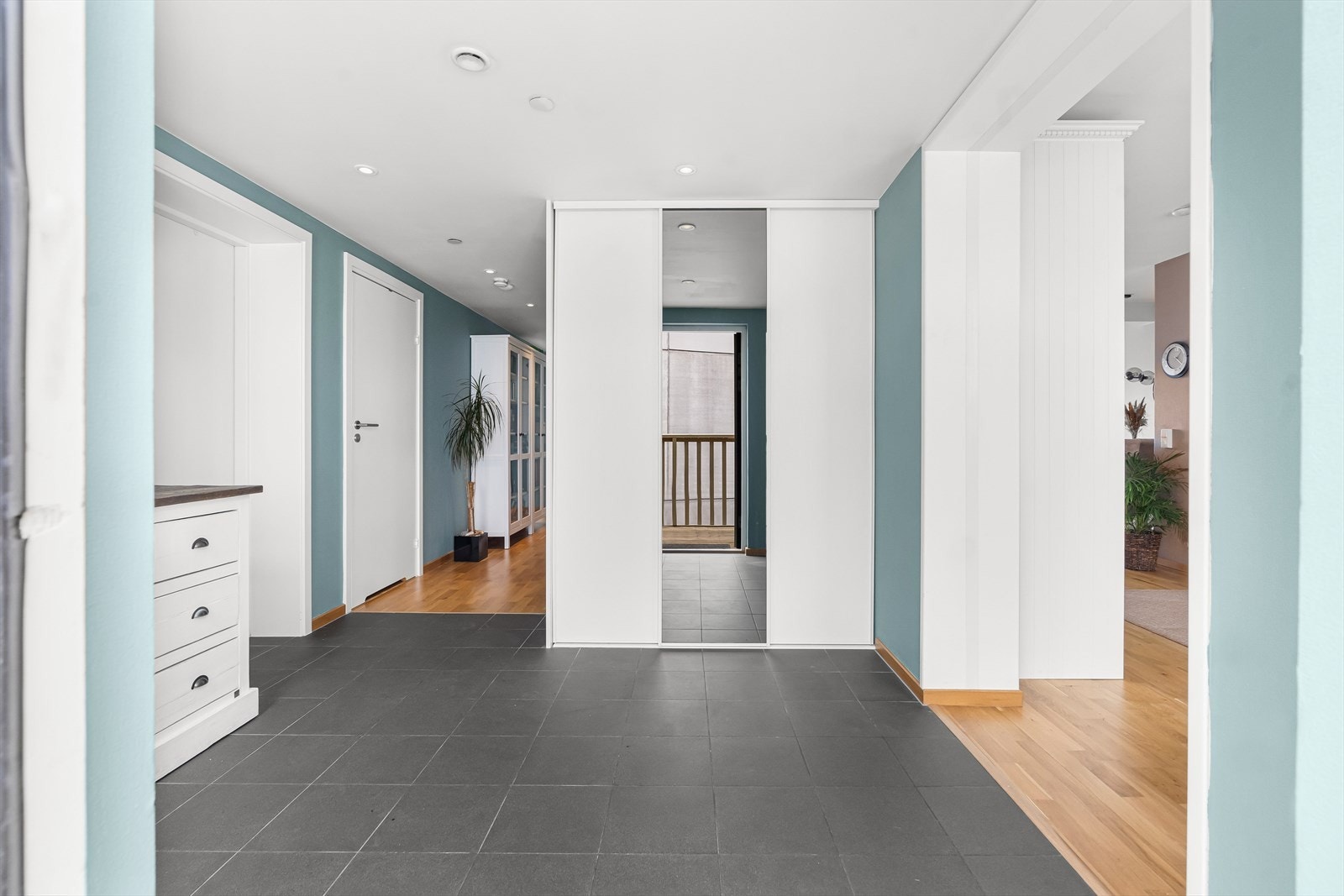 I en hendig nisje er det montert tredørs skyvedørsgarderobe med henholdsvis to hvite, glatte fronter og en front med heldekkende speil. Galleribilde