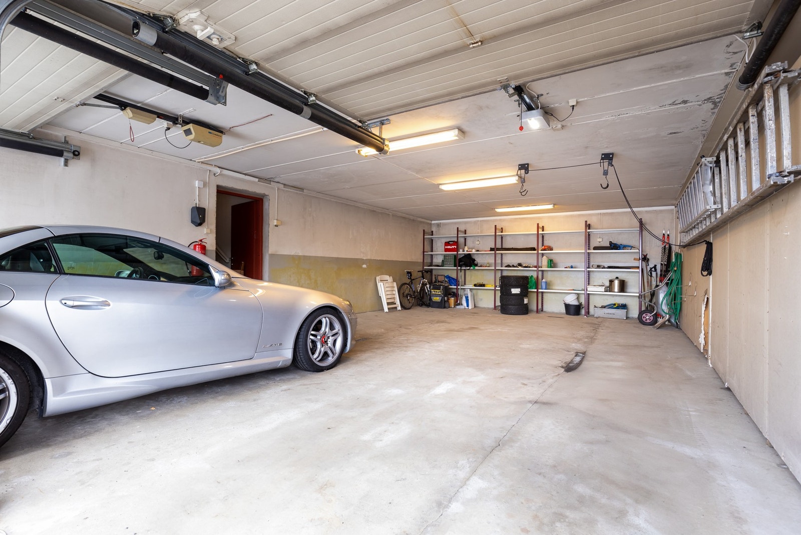 Fra gaten er det innkjøring til garasjen via to garasjeporter. Her er det plass til fire bilder og ytterligere lagringsplass. Galleribilde