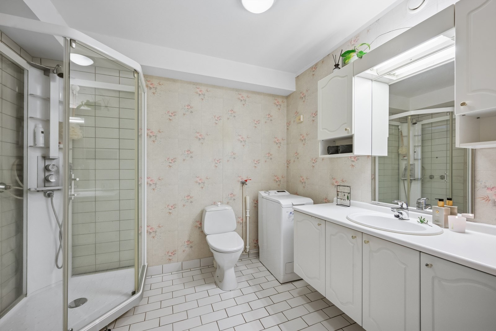 Baderom med flislagt gulv, tapet og sokkelflis på vegg og malt himling. Galleribilde