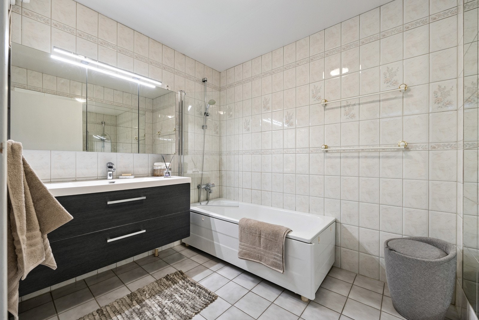 Det 6 kvm store badet er innredet med lyse fliser på vegger og gulv. Pen innredning med romslige skuffeseksjoner, nedfelt servant, speilskap og badekar. Galleribilde