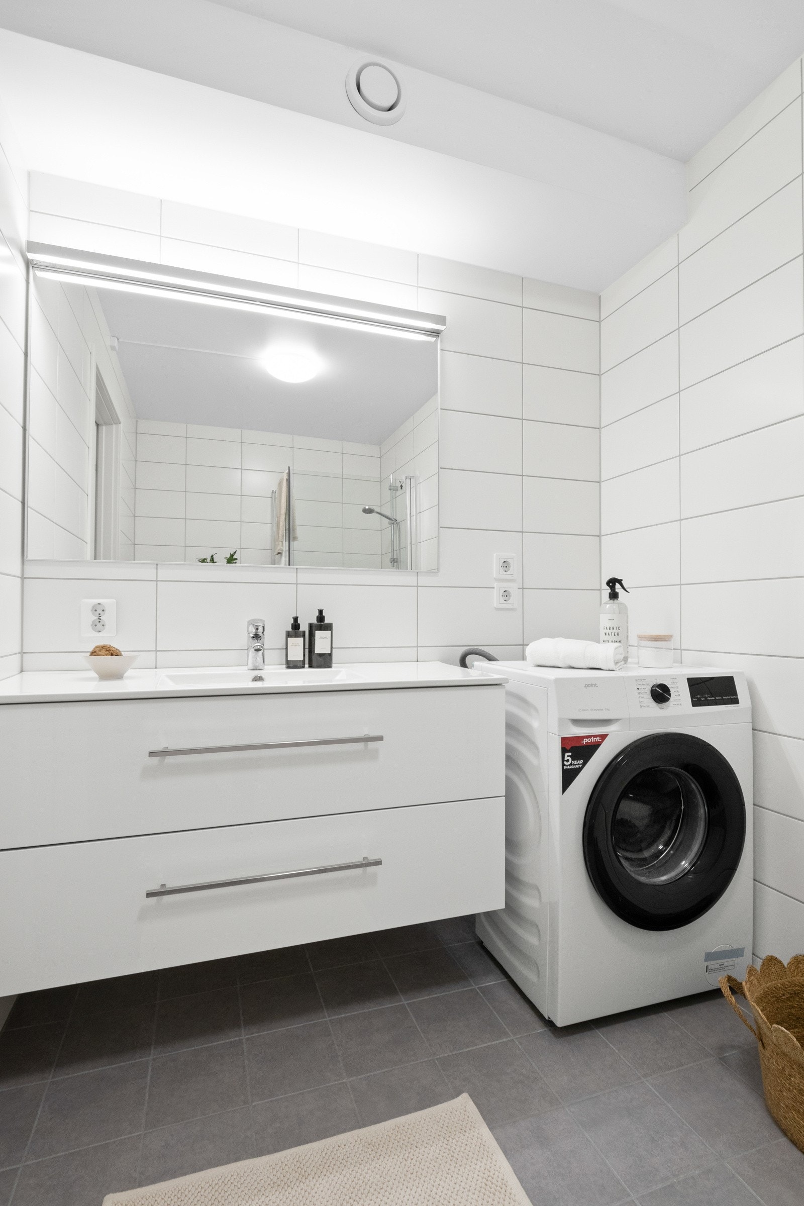 Innredningen består av en heldekkende servant på hvit skuffeseksjon, speil med overlys, et veggmontert toalett og et dusjhjørne med innfellbare glassdører. Galleribilde