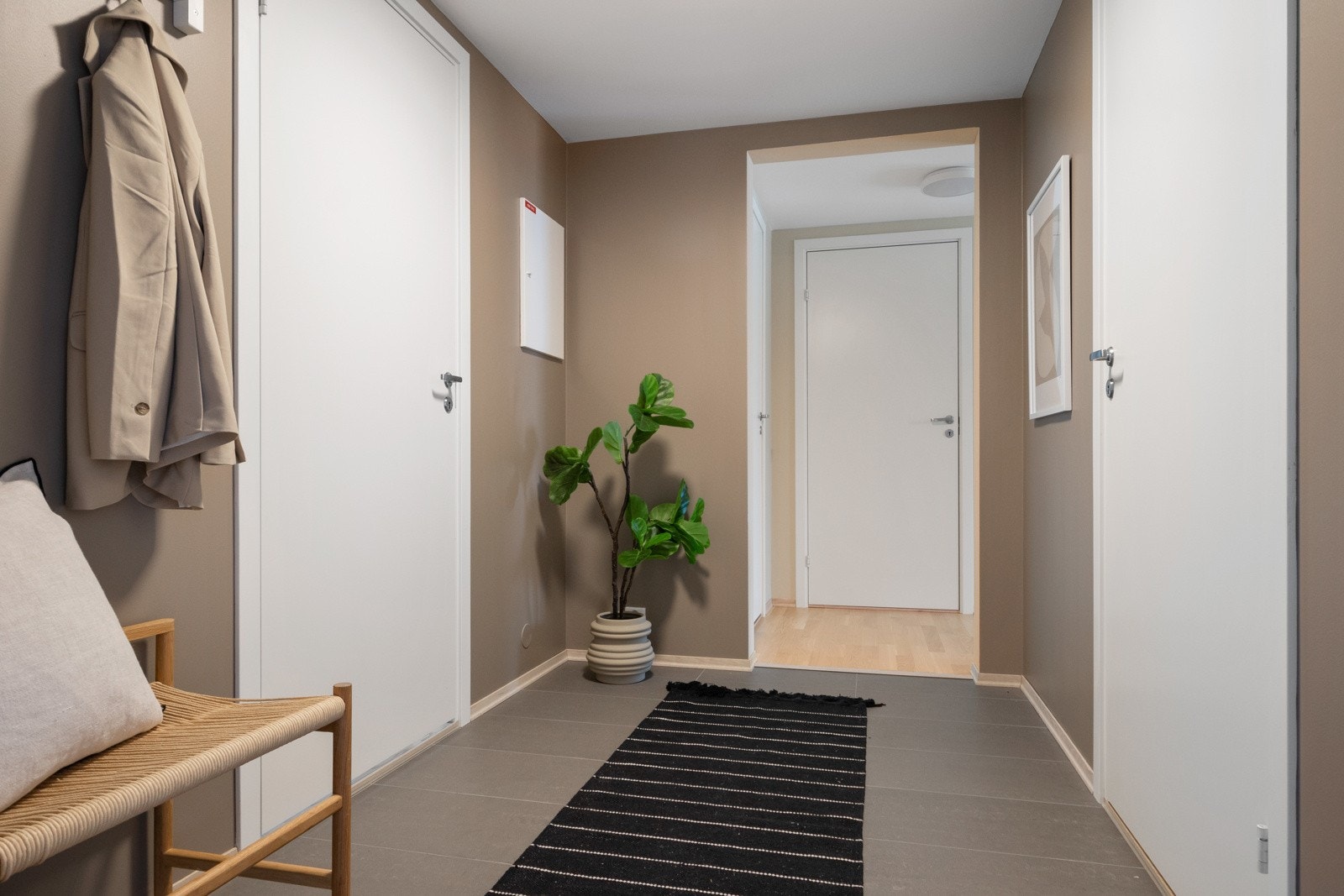 Entreen har fliser på gulv med gulvvarme, listefri himling og glatte vegger malt i en varm jordtone. Galleribilde