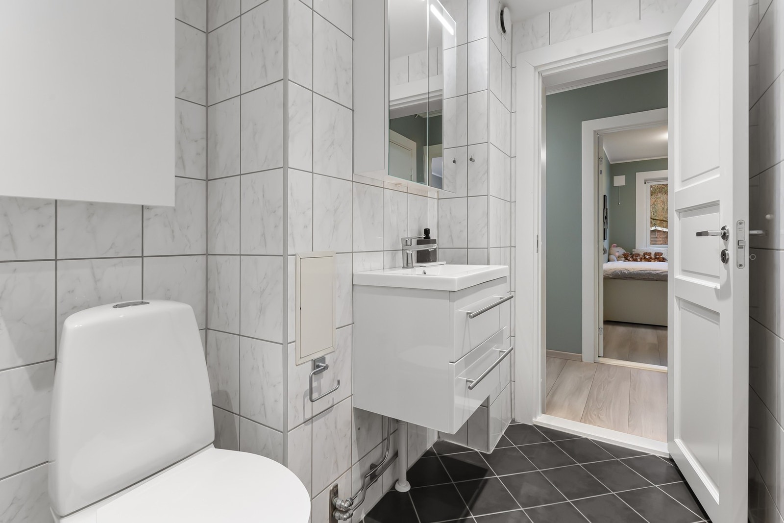 Badet har gulvmontert toalett, samt et dusjhjørne med regnfallsdusj, hånddusj og innfellbare glassvegger. Det er opplegg for vaskemaskin på badet. Galleribilde