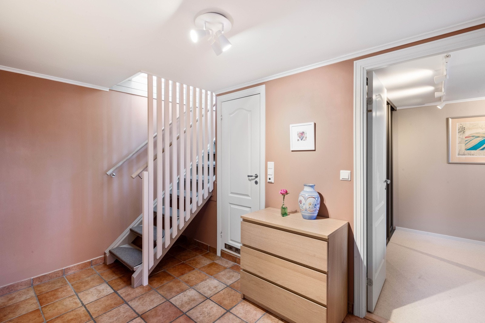 Gang i underetasje med malte vegger med fargen Savanna Sunset og flislagt gulv. Dør til badet og åpen dør til hovedsoverommet. Alle soverommene er plassert i underetasjen i praktisk tilknytning til badet. Galleribilde