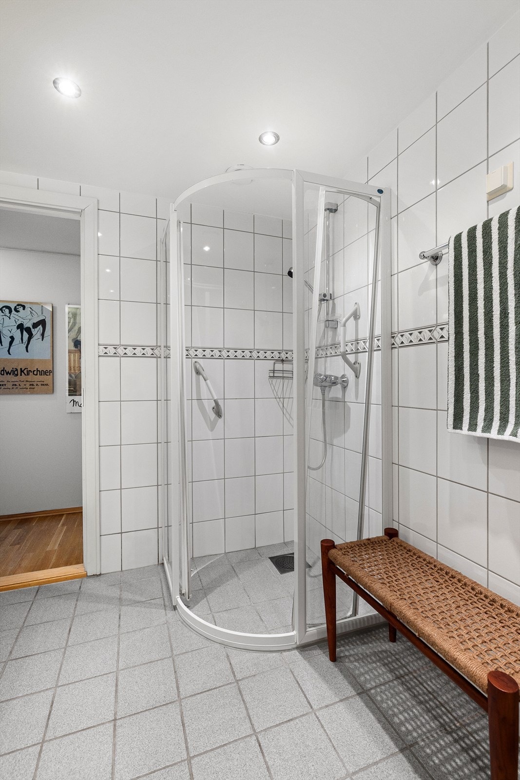 Badet inneholder dusjhjørne med innfellbare dører i glass, toalett og servantskap, nedfelt servant med ett-greps blandebatteri, speil på vegg og belysning. Galleribilde