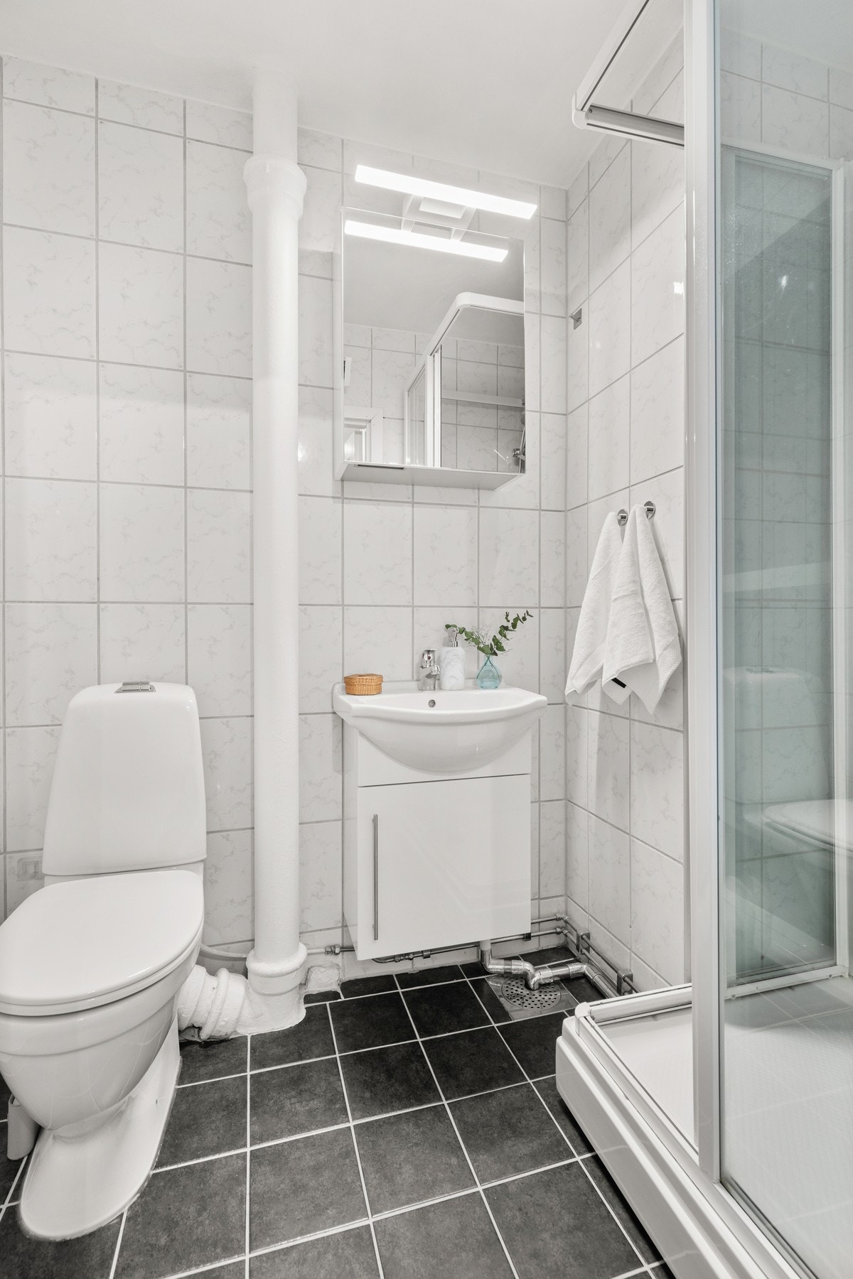 Badet er innredet med hvitt høyglans underskap med servant og overskap med speil, samt ny belysning fra 2024 Galleribilde