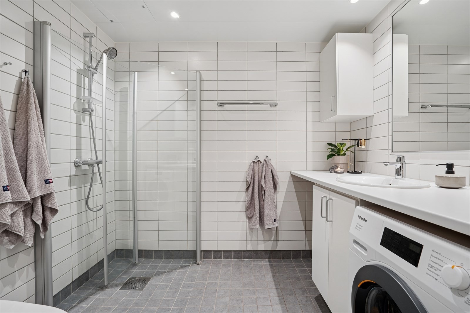 Badet er praktisk innredet og har hvite veggfliser og lysegrå gulv- og sokkelfliser. Galleribilde