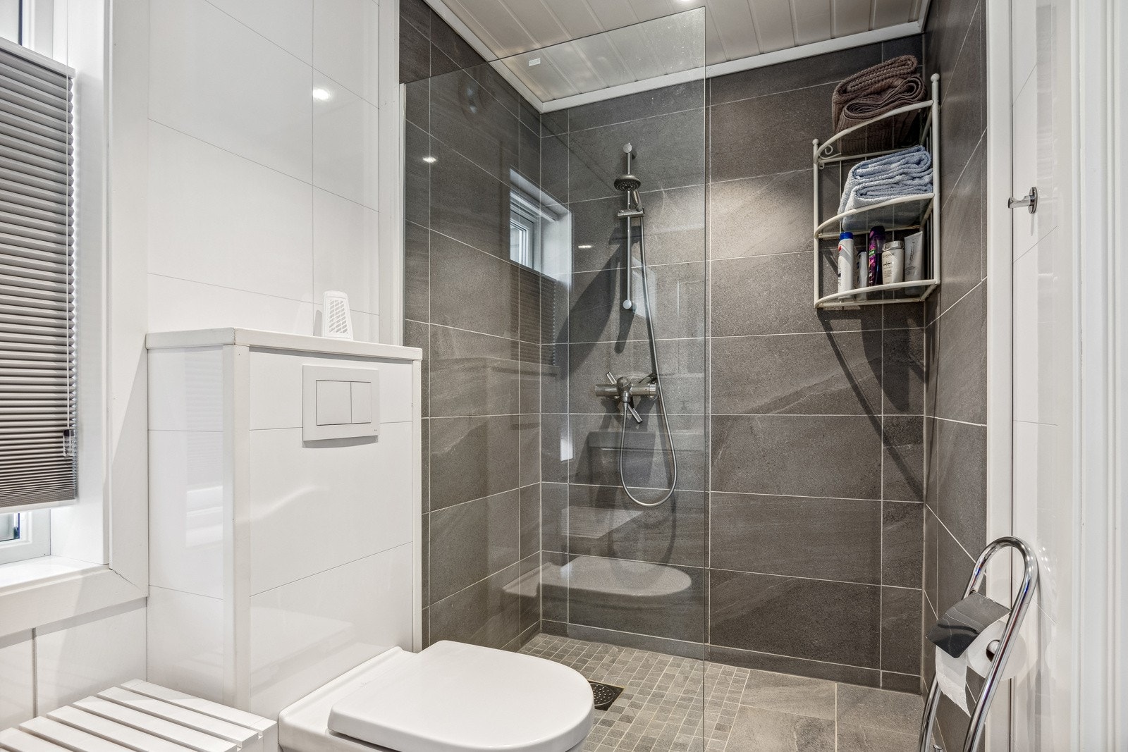 Badet er utstyrt med vegghengt toalett og et helfliset dusjhjørne. Galleribilde