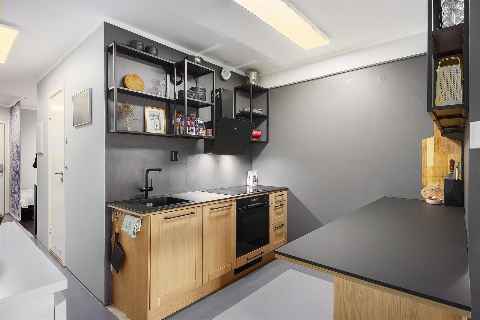 Stilren kjøkkeninnredning med trefronter. Integrert i innredningen er induksjon platetopp, stekeovn, oppvaskmaskin, benkekjøleskap og benkefryser. Galleribilde